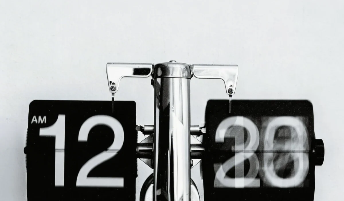 A close-up, black and white shot of a vintage flip clock showing 12:20 AM, with the numbers in mid-flip to illustrate the passage of time.