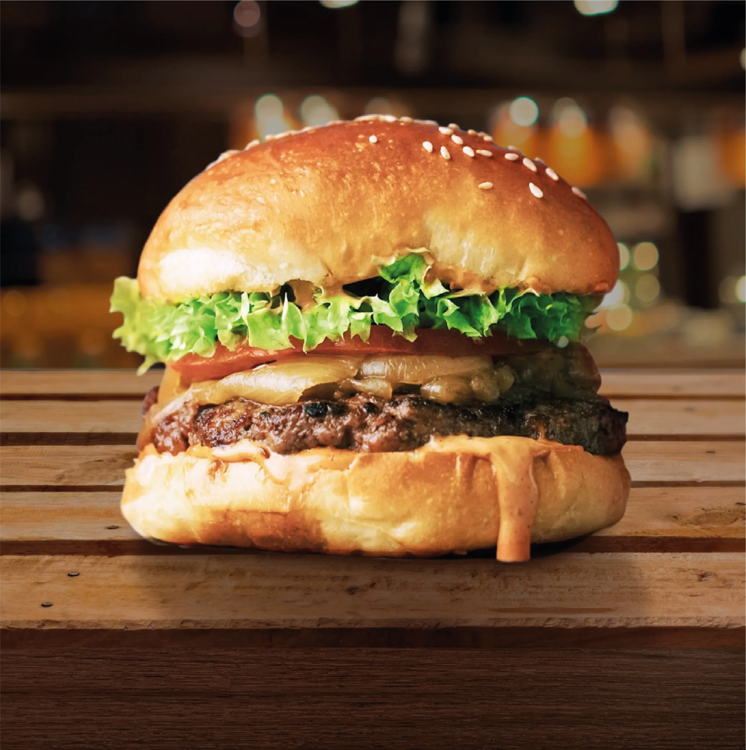 A close-up side view of a juicy beef burger on a toasted sesame seed bun, layered with fresh lettuce, tomato, melted cheese, and a signature sauce on a wooden surface.