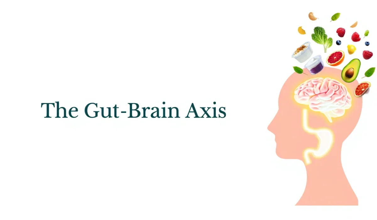 A medical illustration graphic showing a pink silhouette of a human head with a detailed brain and stomach inside. To the right, various healthy whole foods like avocado, spinach, and fruit are floating towards and out of the brain. The text "The Gut-Brain Axis" is on the left against a clean white background.