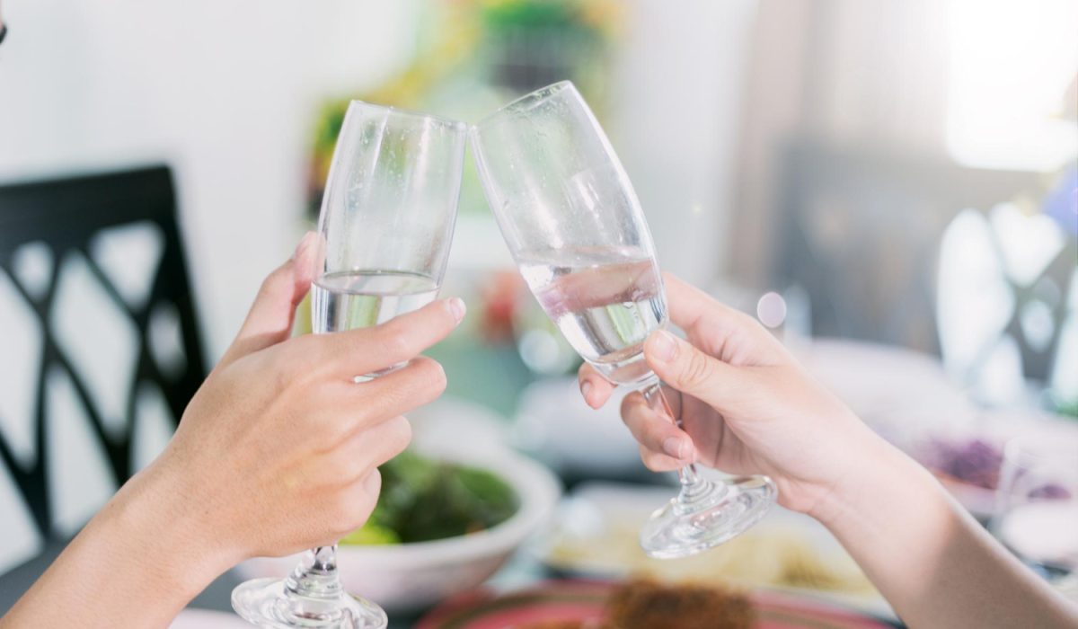 Cropped hands of female friends toasting champagne flutes at dining table