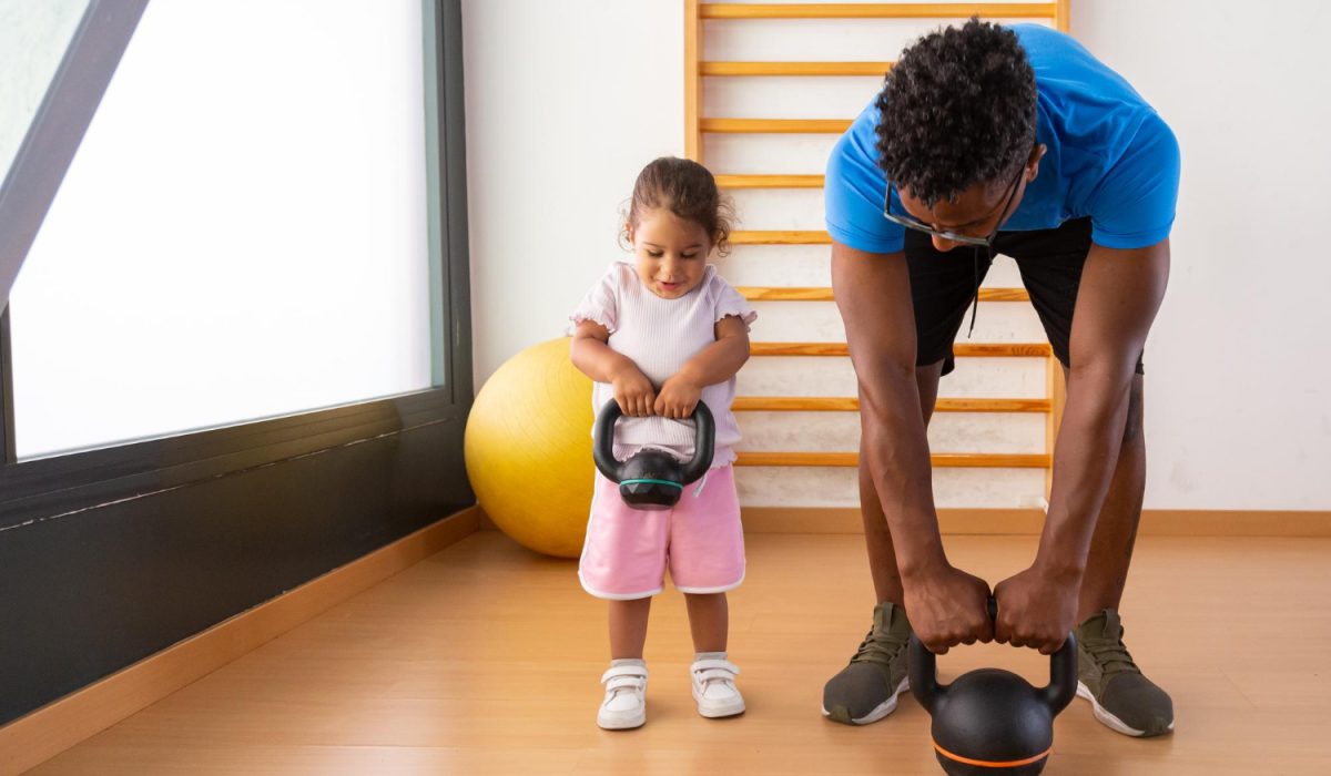 Little kid lifting kettlebell with father