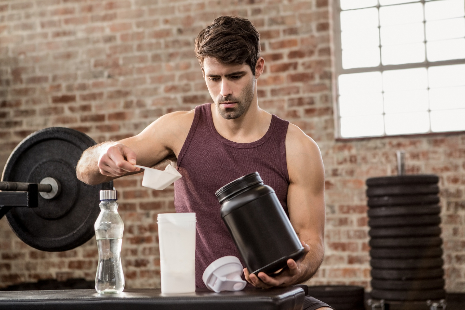 Fit-Guy-Creating-Protein-Shake Man adding supplement from tin to bottle