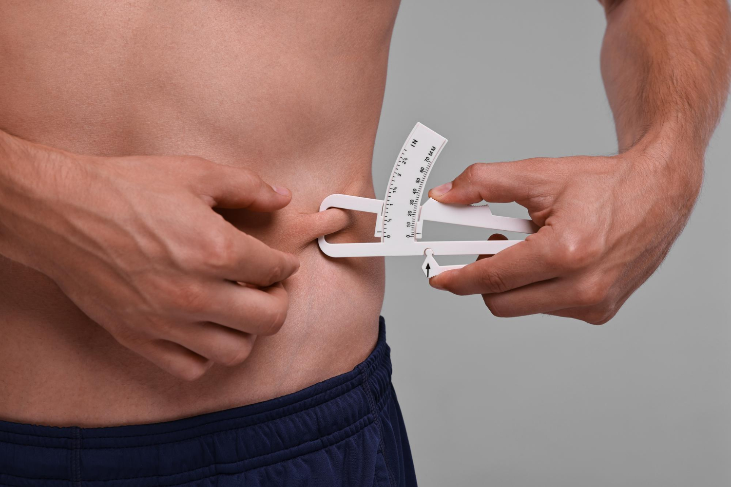 Man measuring body fat with caliper on grey background closeup