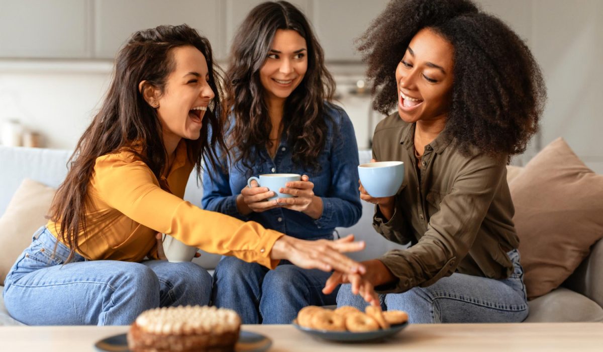 Three joyful multiethnic friends ladies share laughter over coffee indoors