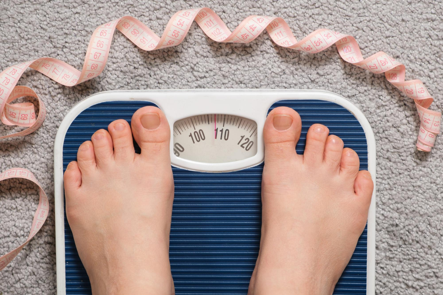 Women's bare feet on floor scales and measuring tape weight