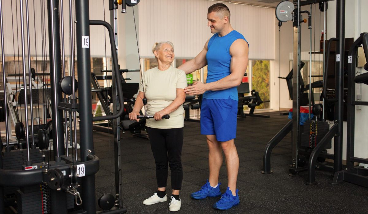 Young handsome coach man helps a pensioner to do an exercise on the