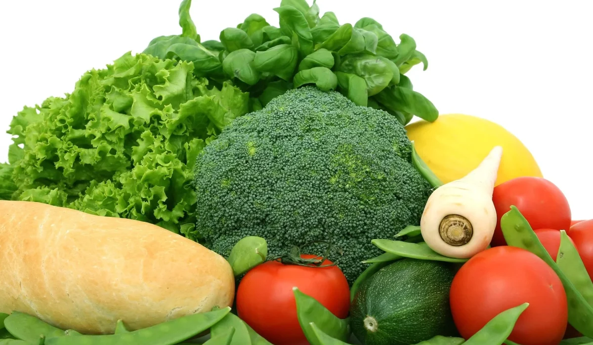 A collection of fresh, whole vegetables including a large head of broccoli, green leafy lettuce, bright red tomatoes, a cucumber, and sugar snap peas against a white background.